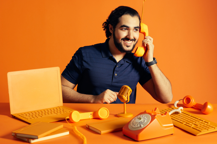 homem sentado em frente a uma mesa cor de laranja segura um telefone sem fio cor de laranja 